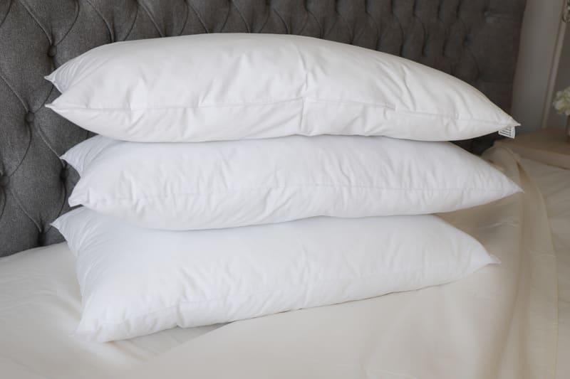 Three plump white pillows stacked in front of a headboard